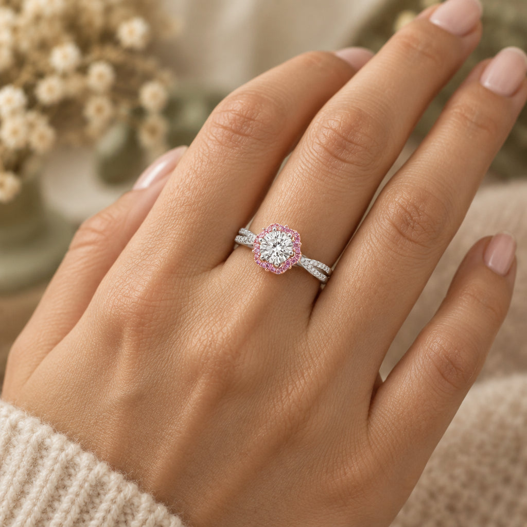 A silver halo ring with a round-cut clear center stone and a border of pink gemstones, displayed on a green velvet ring box.