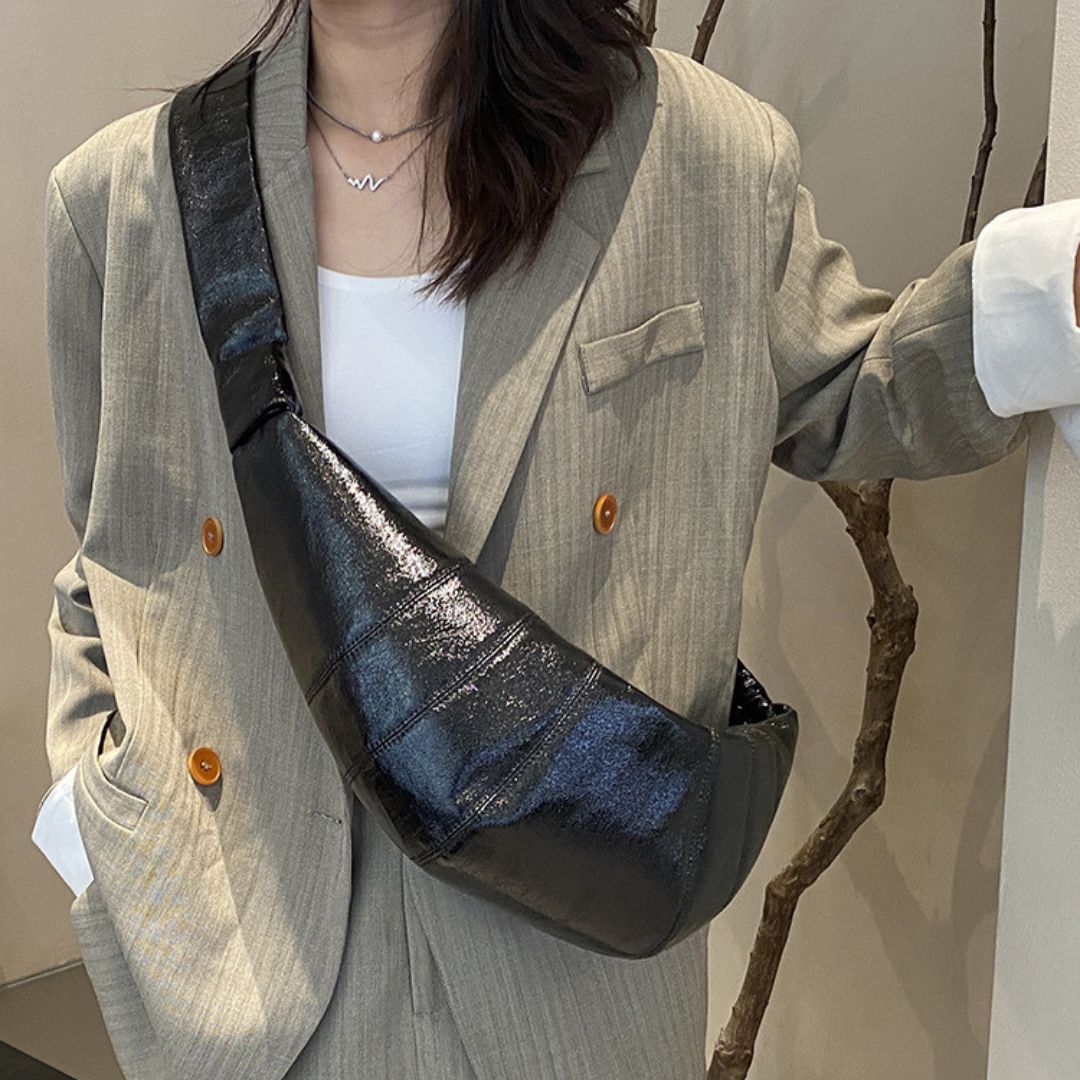 Person wearing a gray blazer with a black crossbody bag featuring blue accents.