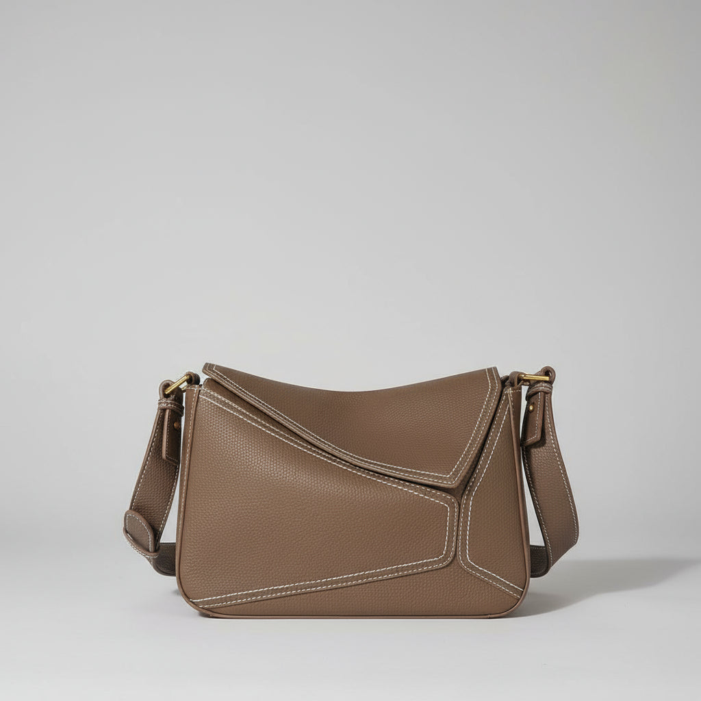 Brown leather handbag on a light surface with plants in the background