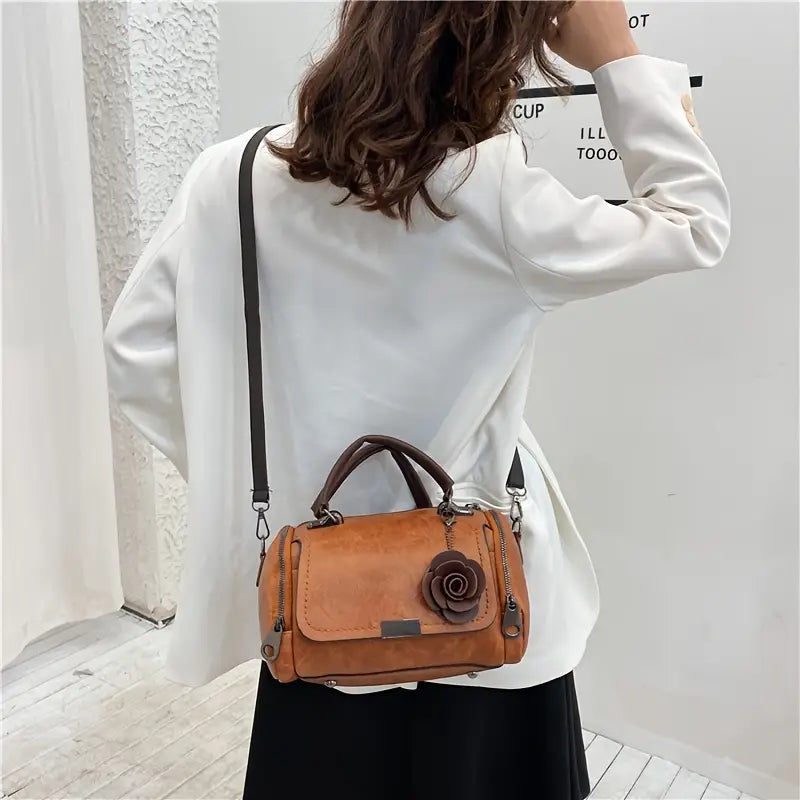 Person wearing a white shirt and carrying a brown leather handbag with a flower detail.