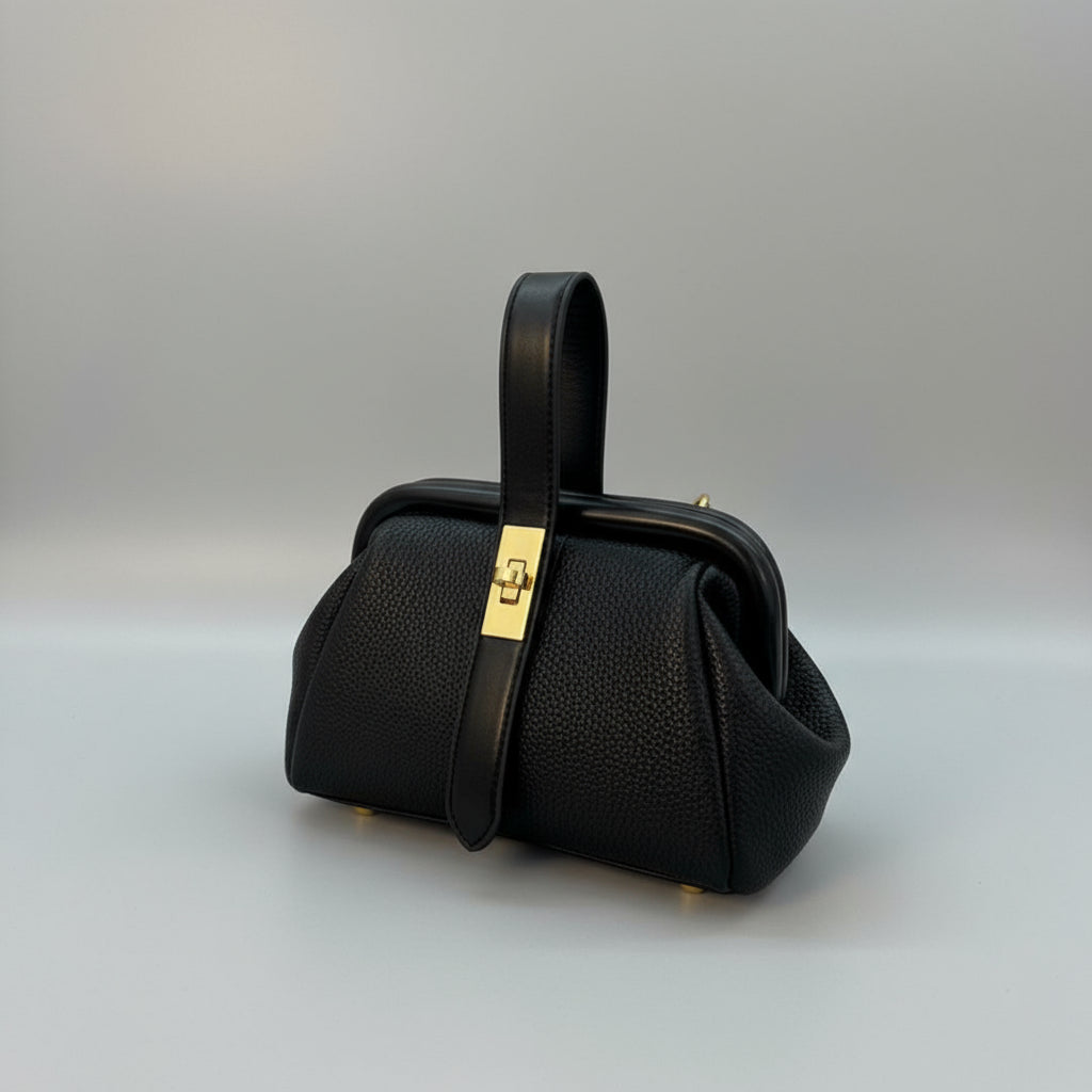 Black handbag with a gold clasp on a white surface with a gray background