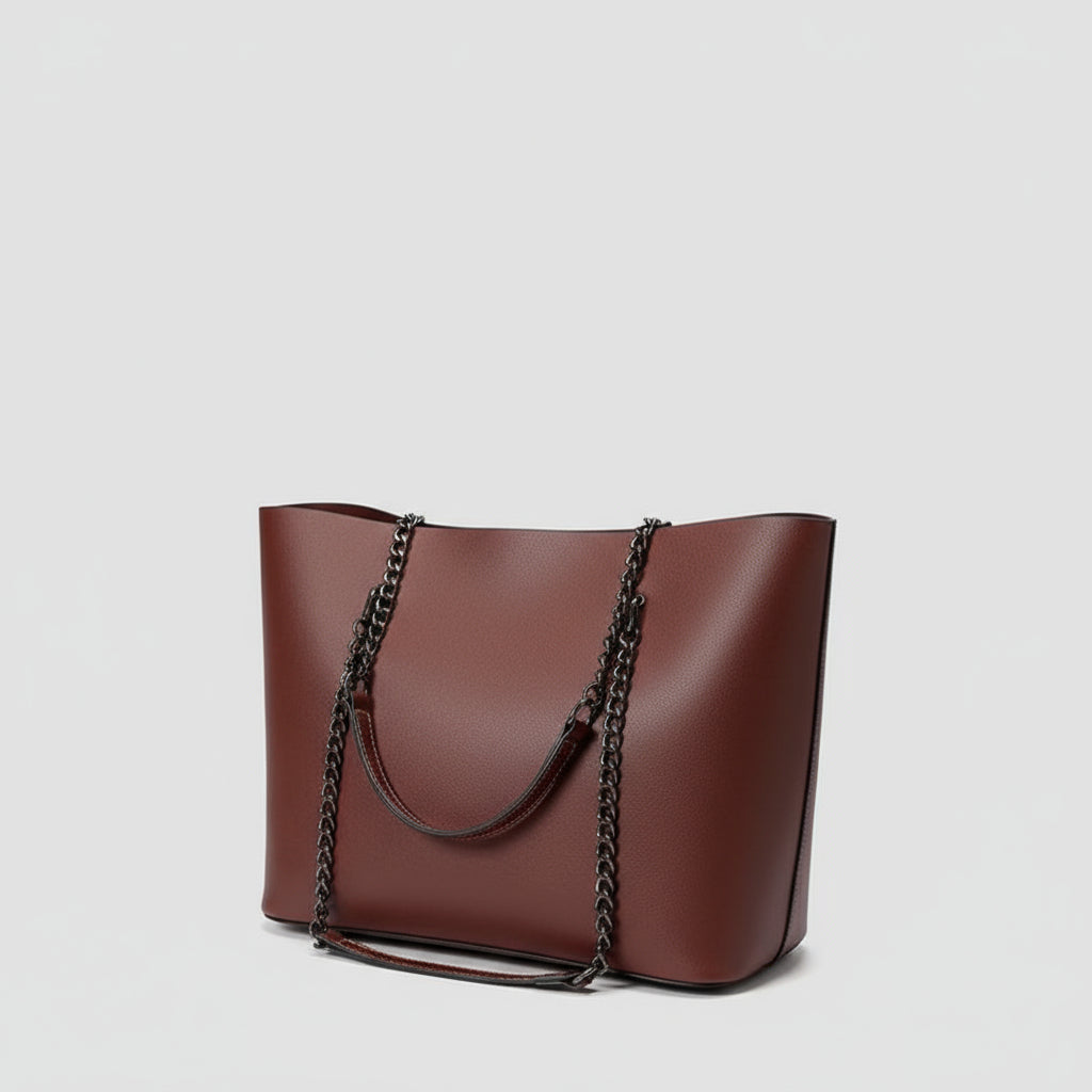 Person holding a brown handbag with a chain detail, wearing a white shirt with black polka dots and blue jeans.