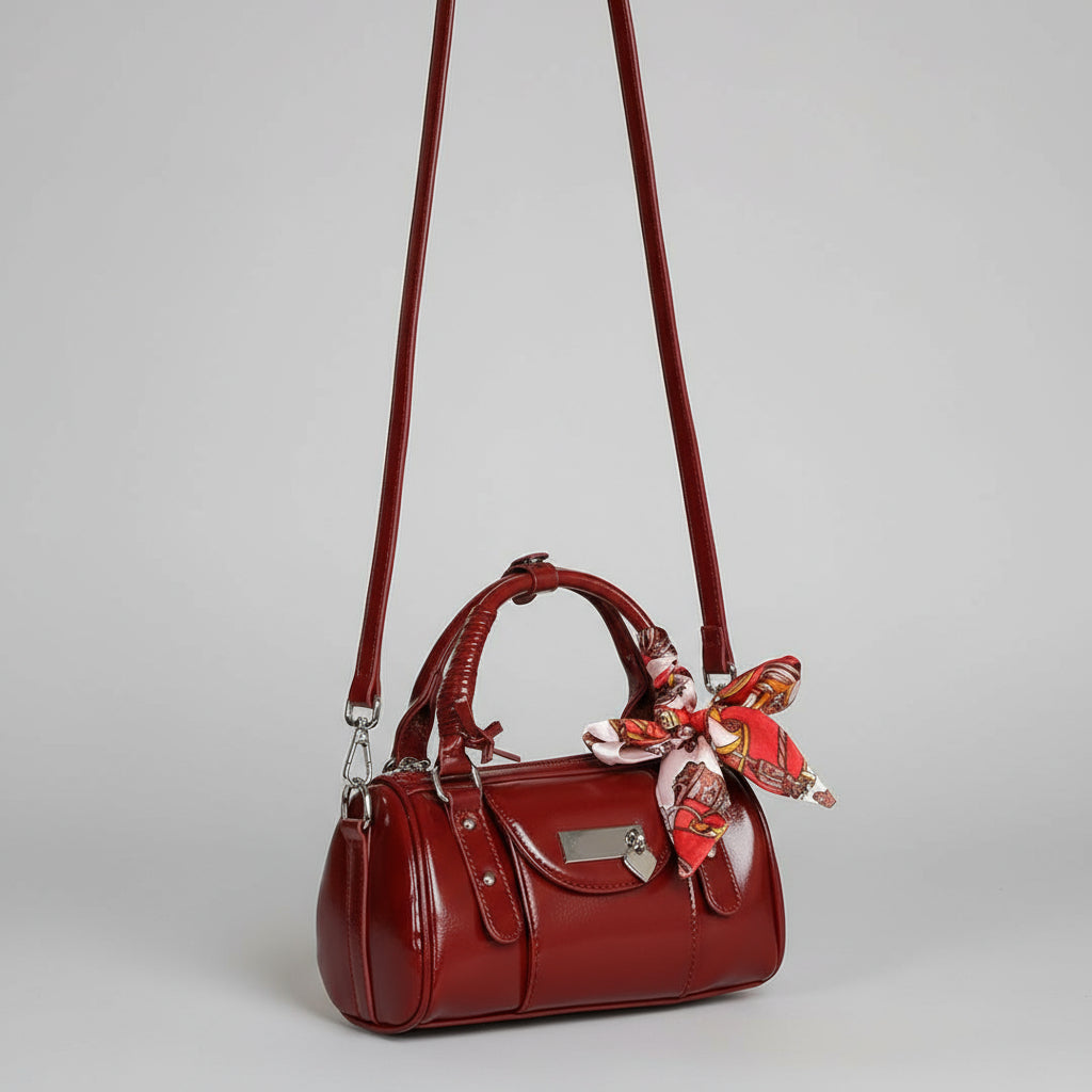 Red handbag with a decorative ribbon held by a person in a white outfit against a beige background