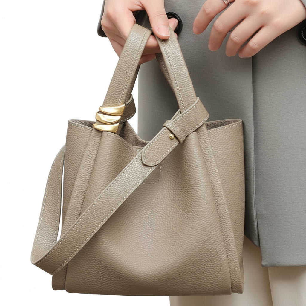 Beige handbag with gold accents held by a person wearing a gray coat.