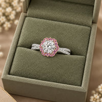 A silver halo ring with a round-cut clear center stone and a border of pink gemstones, displayed on a green velvet ring box.