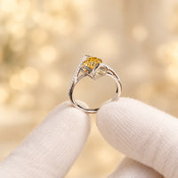 Gold ring with a yellow gemstone held by a hand against a blue box background