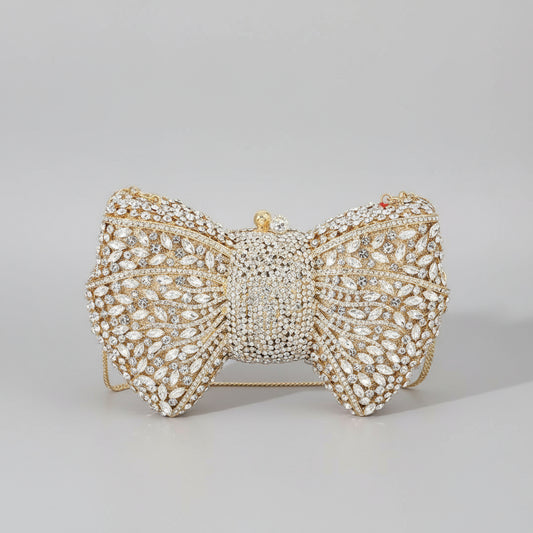 Gold bow-shaped clutch bag with crystal embellishments on a white surface.