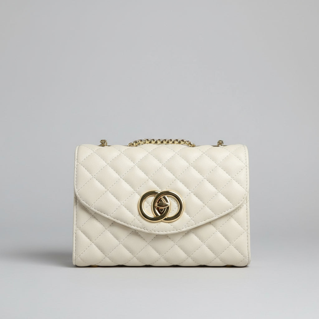 White quilted handbag with gold chain held by a hand against a white background