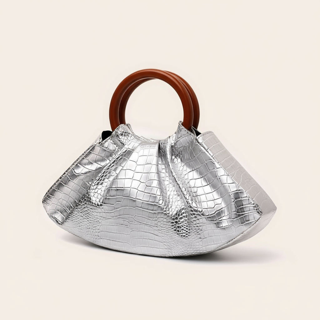 Silver metallic handbag with a brown handle on a light beige background
