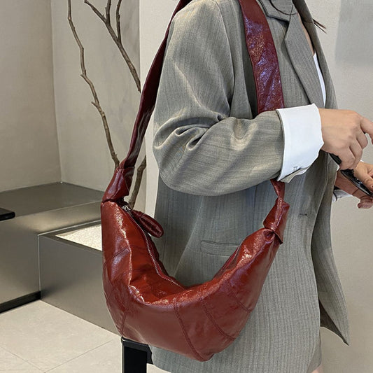 Person wearing a gray coat holding a brown leather handbag indoors.