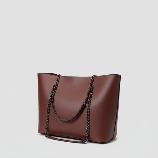 Person holding a brown handbag with a chain detail, wearing a white shirt with black polka dots and blue jeans.