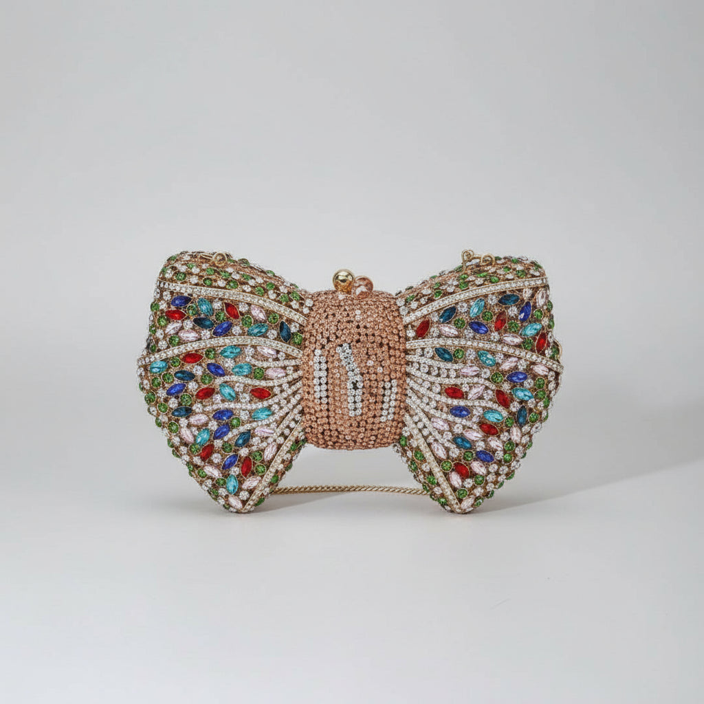 Decorative butterfly-shaped handbag with colorful gemstones on a white surface with a plant and vase in the background.