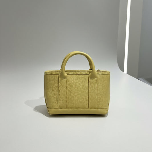 Yellow handbag with a strap held by a hand on a light gray background