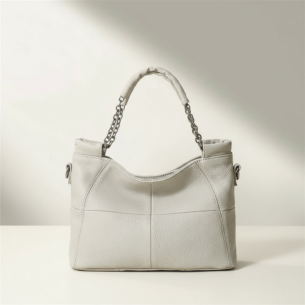 Beige handbag with chain handle on a light surface with a neutral background