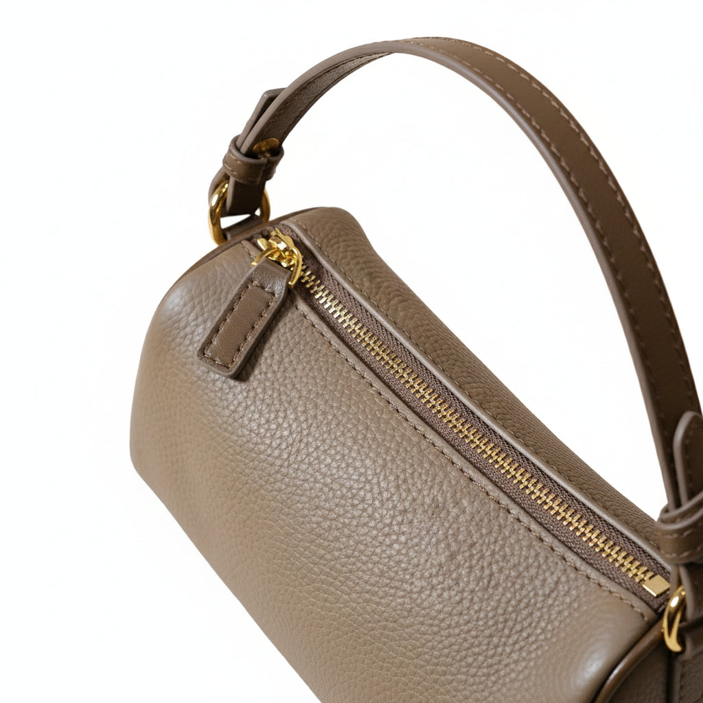 Close-up of a brown leather handbag with a gold zipper and clasp on a beige background