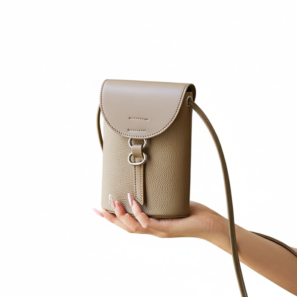 Beige leather handbag held by a hand against a neutral background