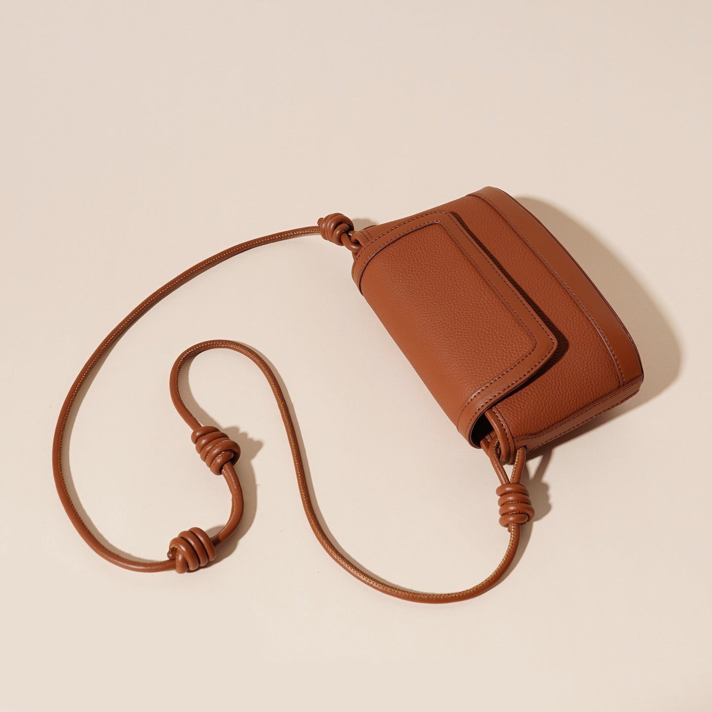 Brown leather crossbody bag on a beige background