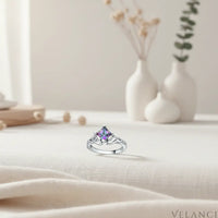Silver ring with a colorful gemstone on a light fabric surface with decorative vases in the background | Velanci Womens Ring