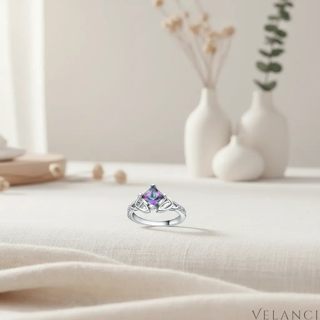 Silver ring with a colorful gemstone on a light fabric surface with decorative vases in the background | Velanci Womens Ring
