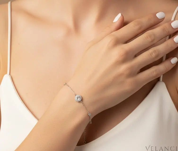 Close-up of a hand wearing a silver bracelet with a clear gemstone on a neutral background