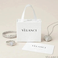 Velanci jewelry set including a heart-shaped pendant, ring, and bracelet on a beige background.