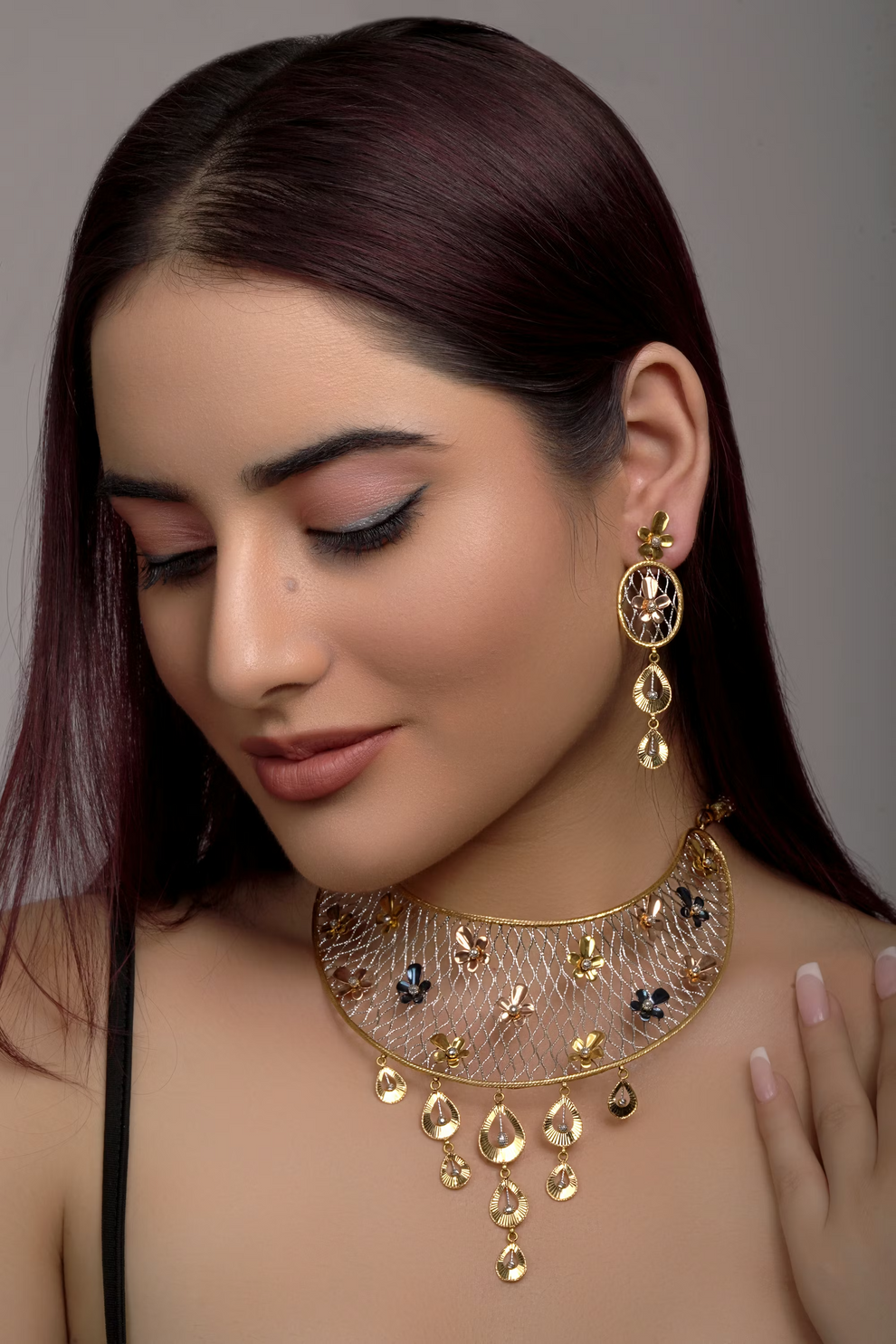 Woman wearing a gold necklace and earrings against a gray background