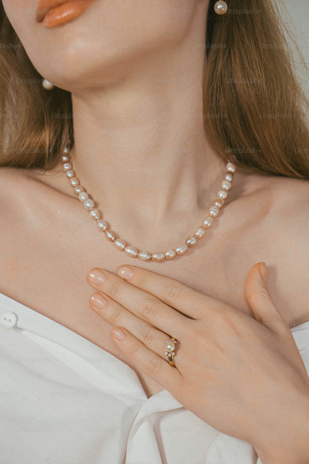 Close-up of a woman wearing a pearl necklace and ring, with a blurred background.